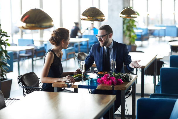 Gelukkig man in pak praten met zijn vriendin door romantische lunch in modern restaurant - Foto, afbeelding