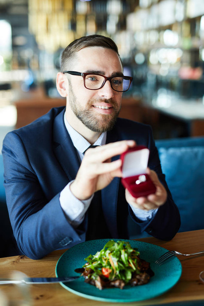 Happy young man showing engagement ring to his girlfriend by lunch in restaurant - Photo, image