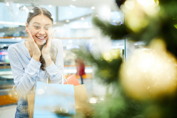 Joven comprador asombrado mirando el árbol de Navidad decorado en el escaparate mientras pasa tiempo en el centro comercial
 - Foto, Imagen