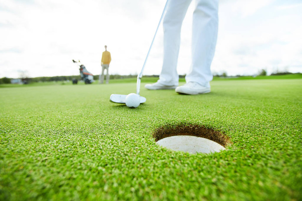 Giocatore di golf che tiene il randello vicino alla sfera prima di colpire mentre mira al foro
 - Foto, immagini