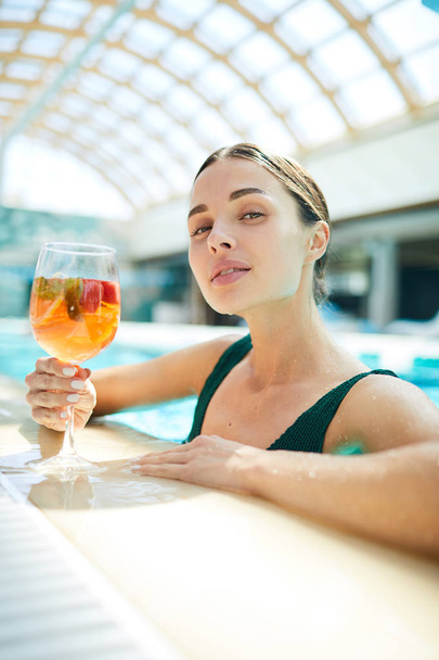 Giovane donna riposante con cocktail di frutta seduta in piscina nel moderno centro benessere o resort
 - Foto, immagini