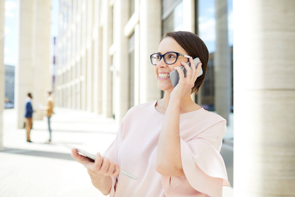Empresária feliz com smartphone consultando seus clientes ao ar livre com colegas em segundo plano
 - Foto, Imagem