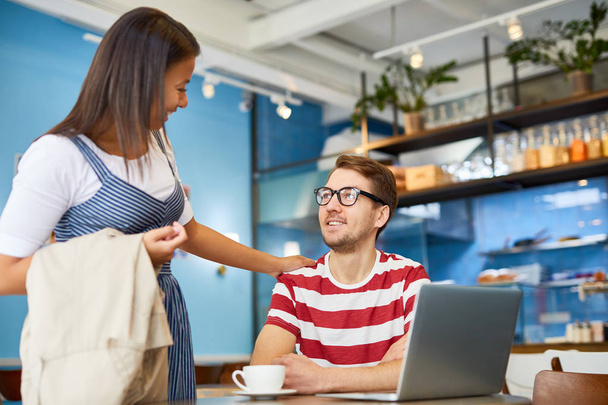 Jonge vrouw met loopgraaf rond arm ontmoeten haar collega in cafe tijdens koffie-break - Foto, afbeelding