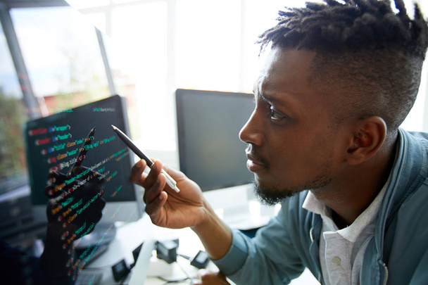 Serious concentrated young African-American programmer looking confused while learning coding language himself - Foto, imagen