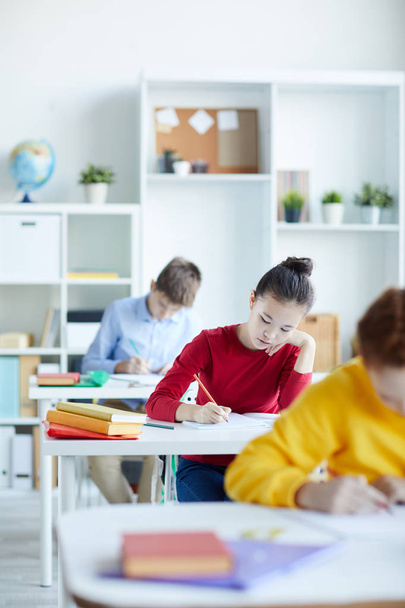 Fleißige Schülerin macht sich Notizen in Textbuch, während sie am Schreibtisch zwischen ihren Klassenkameraden sitzt - Foto, Bild
