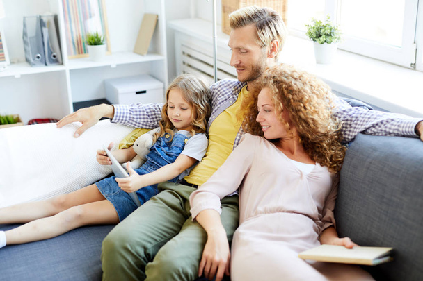 Kleine dochter toont haar ouders nieuwsgierig video in Tablet tijdens familie rust in de woonkamer - Foto, afbeelding