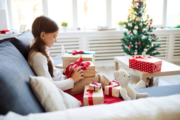 Счастливый ребенок сидит на диване и распаковывает коробки с рождественскими подарками
 - Фото, изображение