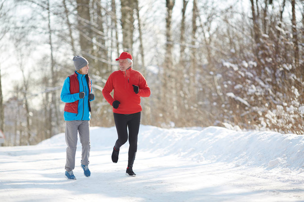 凍りつくような朝に冬の森で雪道走ってスポーツウェアのアクティブ シニア カップル - 写真・画像