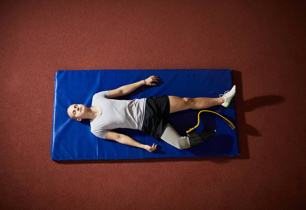 Fiatal nyugodt paralimpiai sportoló-val fogpótlás a jobb lábát feküdt szőnyeg, mielőtt játék - Fotó, kép