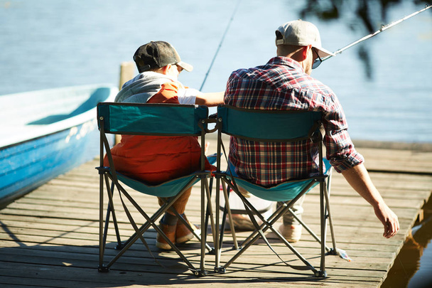 Vue arrière de père et fils pêchant ensemble sur une jetée dans la journée d'été
 - Photo, image