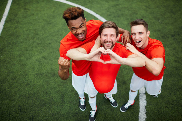 Kolme nuorta jalkapallon mestaria univormussa seisoo kentällä samalla kun he ilmaisevat voittoaan
 - Valokuva, kuva
