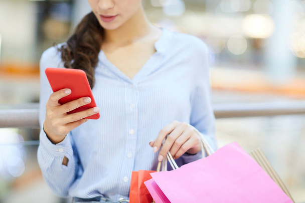 Молодий покупець зі смартфонами та паперовими мішками прокручує нові повідомлення та сповіщення після покупок
 - Фото, зображення