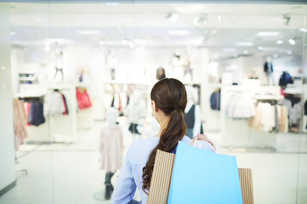 Rückansicht von jungen Shoppern mit Papiertaschen, die während des saisonalen Verkaufs die Kleiderabteilung in einem großen Einkaufszentrum besuchen - Foto, Bild