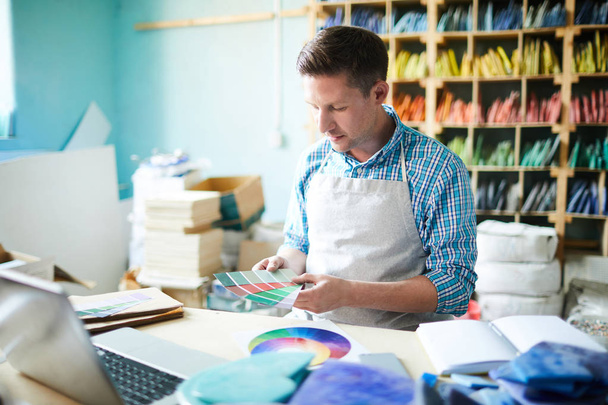 Portrait d'un artisan moderne choisissant une palette de couleurs tenant des échantillons assis à table dans un atelier moderne, espace de copie
 - Photo, image