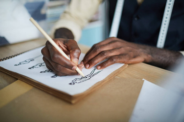 Ręce afrykańsko-amerykańskiego projektanta mody z ołówkiem tworzenia szkiców nowych modeli na papierze - Zdjęcie, obraz