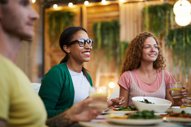 Dos chicas interculturales felices sentadas junto a una mesa festiva en la cena y hablando
 - Foto, imagen