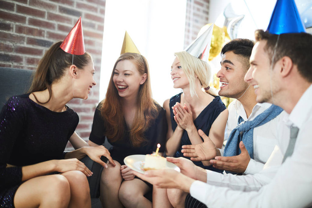 Ομάδα των νεαρών χαρούμενοι φίλοι σε καπέλα γενεθλίων Γιορτάζοντας την επέτειο ενός από τα κορίτσια στο σπίτι κόμμα - Φωτογραφία, εικόνα