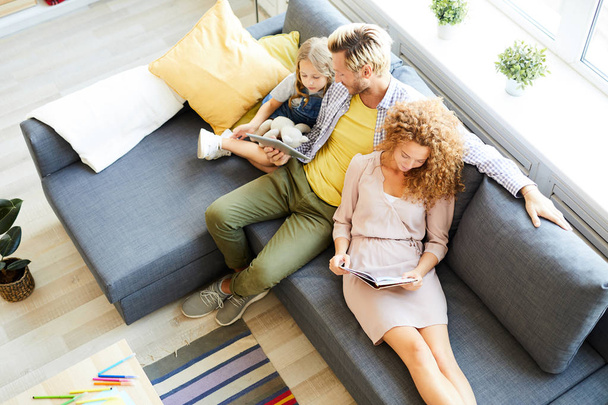 Aperçu de la famille détendue de trois assis sur le canapé, lire et regarder un film en ligne le week-end
 - Photo, image