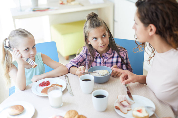 Petites filles mignonnes mangeant un repas fait maison pour le petit déjeuner avec leur mère à proximité
 - Photo, image