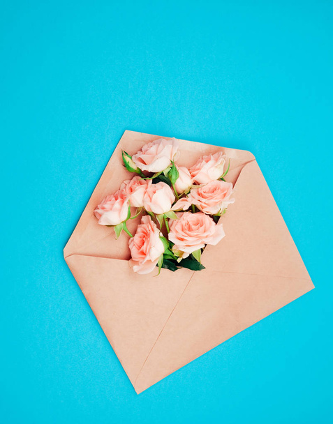 Love or valentine's day concept. Red beautiful roses in envelope on a wooden background. Top view - Foto, Imagem