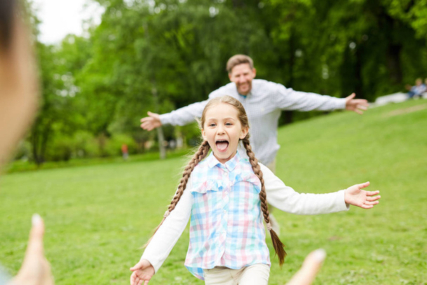 fröhliches und lustiges kleines Mädchen rennt zu ihrer Mutter, während sich ein junger Mann hinter ihr bewegt - Foto, Bild