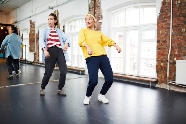 Two young active women doing hip hop exercises on the floor with large mirror on background - Foto, Bild