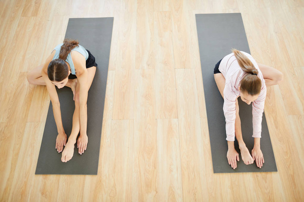 Duas meninas flexíveis esticando os braços para a frente com uma perna esticada e a outra dobrada durante o treino em esteiras
 - Foto, Imagem
