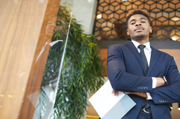 現代のオフィスで文書と一緒に立ってフォーマルな服を着た自信のある若いアフリカのビジネスマンの肖像画 - 写真・画像