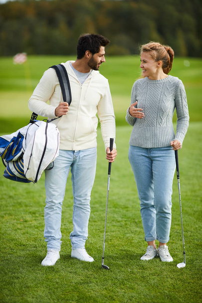 feliz jovem casal ativo com tacos de golfe discutindo lugar onde jogar
 - Foto, Imagem