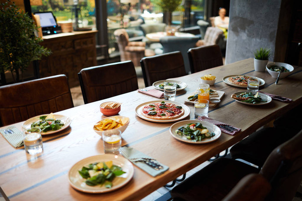 Mesa de madera en la cafetería o restaurante servido con ensalada, pizza y otros aperitivos para los huéspedes
 - Foto, Imagen