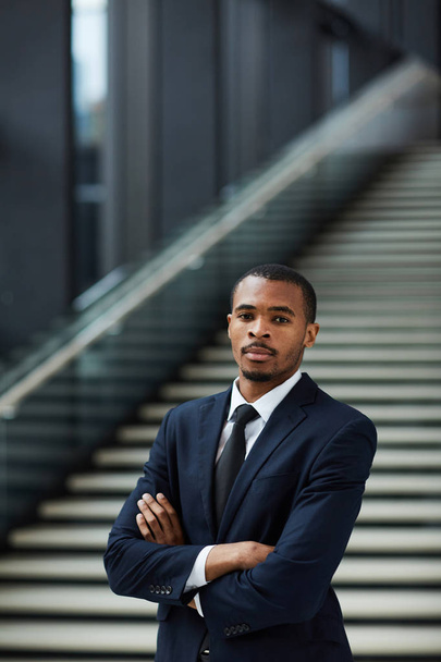 Young cross-armed businessman of African-american ethnicity standing by staircase in lounge - Foto, immagini