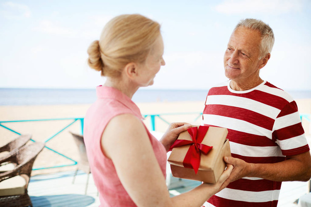 Femme mûre ouvrant boîte cadeau de son mari tout en le regardant et en disant merci
 - Photo, image