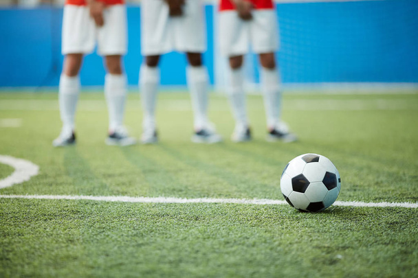 Μπάλα ποδοσφαίρου σε πράσινο ποδοσφαιρικό γήπεδο από τη διαχωριστική γραμμή και τα πόδια τρεις παίκτες σε φόντο - Φωτογραφία, εικόνα