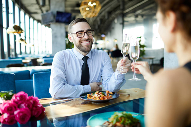 Fiatal vidám férfi csengő a fuvola, hogy az ő barátnője több mint szolgált asztal romantikus időpontban az étteremben - Fotó, kép