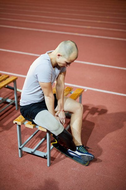 Jovem desabilitar desportista com perna direita artificial sentado no banco no estádio antes ou depois do jogo
 - Foto, Imagem