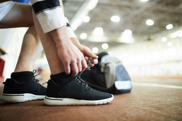 Современный спортсмен, завязывая шнурки на кроссовки при подготовке к тренировкам на стадионе
 - Фото, изображение