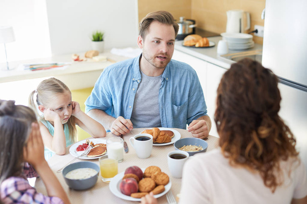 Nervioso marido hablando con su esposa en el desayuno con sus dos pequeñas hijas sentadas cerca
 - Foto, Imagen
