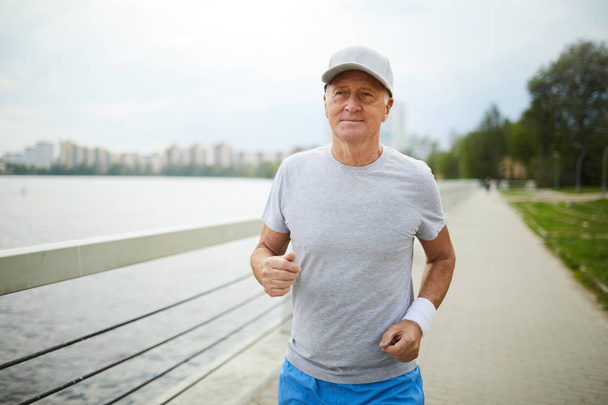 Активний старший чоловік у спортивному одязі практикує біг у міському середовищі вранці
 - Фото, зображення