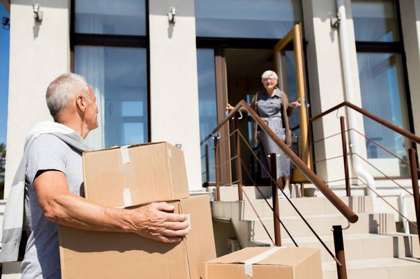 Retrato de pareja mayor moderna descargando cajas de cartón mientras se muda a una nueva casa, céntrese en el hombre en frente
 - Foto, Imagen
