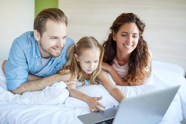 Giovane famiglia di tre sdraiati sul letto con perno lapto davanti e guardare film nel fine settimana
 - Foto, immagini
