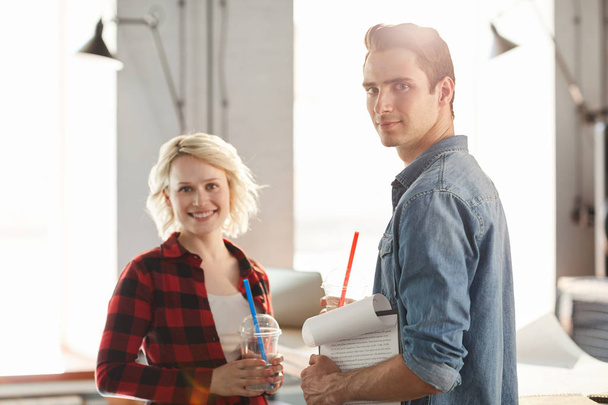 Portrait of two young business people wearing casual clothes smiling happily looking at camera while working in modern office, focus on handsome man in front, copy space - Φωτογραφία, εικόνα