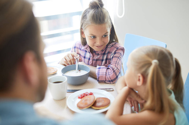 Een van de schattige meisjes iets te zeggen aan haar zus terwijl het eten van muesli met melk voor het ontbijt - Foto, afbeelding