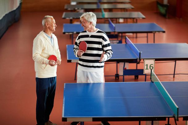 Deux sportifs à la retraite en tenue décontractée debout à côté de la table de tennis tout en discutant de quelques moments
 - Photo, image