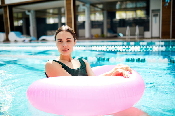 ピンクのプール ブイのスパリゾート ホテルで泳ぎながらカメラ目線で若いゆっくり女性 - 写真・画像