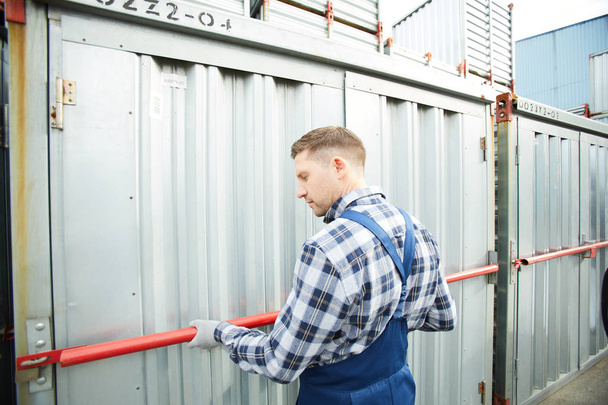 Arbeiter in Overalls überprüfen Sicherheitsbügel, während er einen der Lagercontainer schließt - Foto, Bild