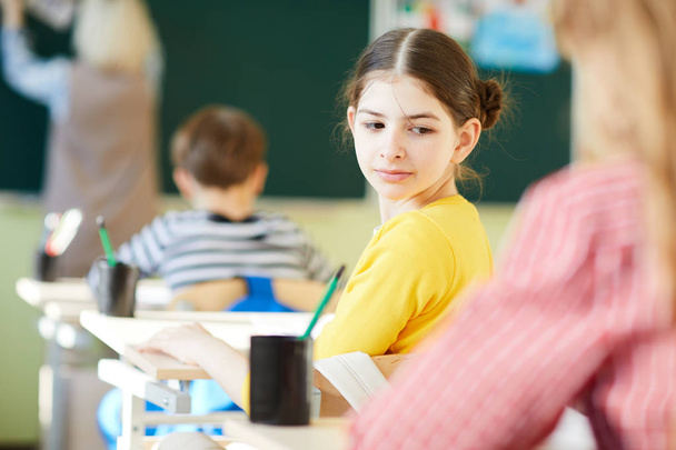 Estudante bonita morena curiosa em camisola amarela se voltando enquanto trai colega de classe durante o exame escolar
 - Foto, Imagem