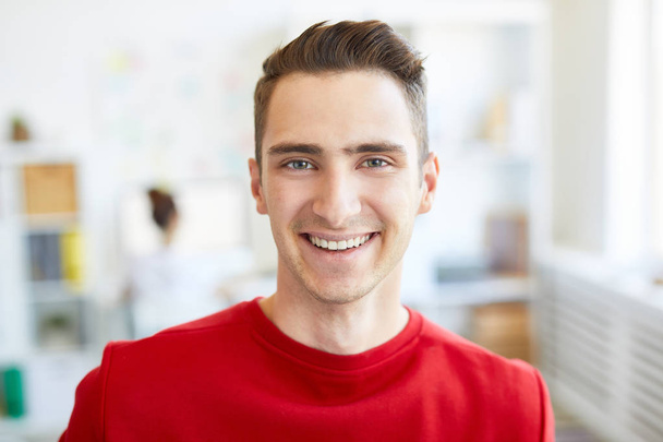 Szczęśliwy facet w czerwonym dorywczo sweter patrząc na Ciebie z Toothy uśmiech podczas przerwy w biurze - Zdjęcie, obraz