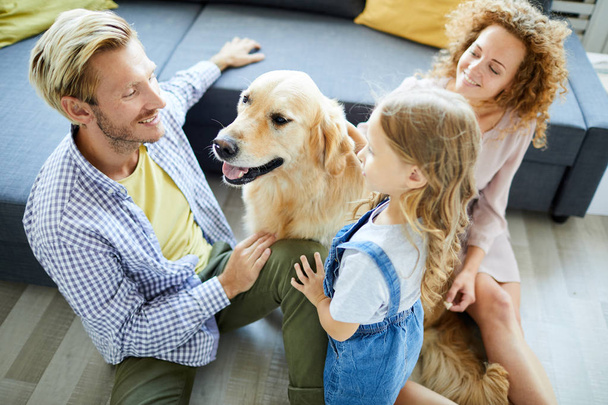 Jonge familie van drie zitten op de vloer per bank, praten en spelen met huisdier - Foto, afbeelding