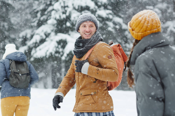 Sorridente bel giovane escursionista in cappello e sciarpa tornando a parlare con l'amico mentre camminano in fila durante l'escursione invernale
 - Foto, immagini