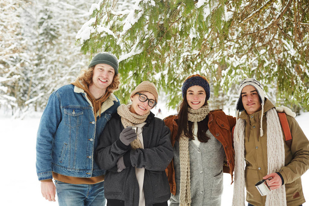 Cintura até retrato de grupo de jovens felizes posando em resort de inverno de pé sob o abeto na bela floresta nevada
 - Foto, Imagem